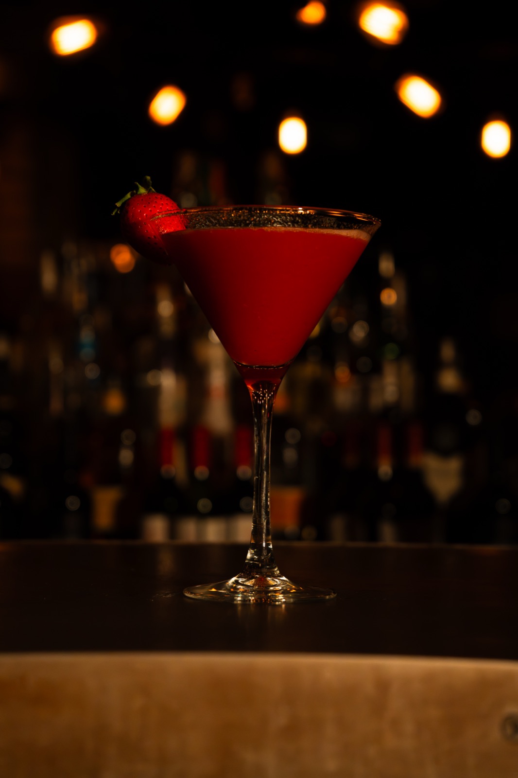 A deep red martini on the bar under warm lights