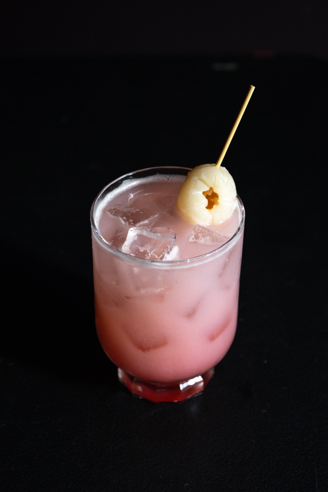 A pink lychee cocktail garnished with a whole lychee